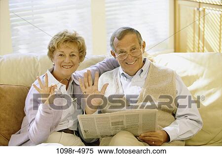 Stock Photography - Portrait of a senior couple sitting on a couch waving to the camera. Fotosearch