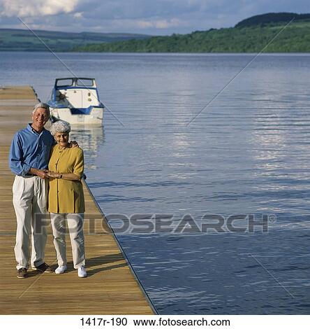 Stock Image - Portrait of a senior couple standing on a pier, Loch Lomond, Scotland. Fotosearch