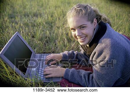 Stock Image - Portrait of a teenage girl lying on a lawn using a laptop. Fotosearch