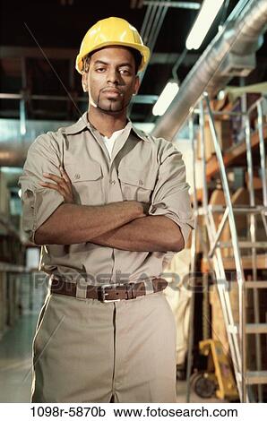 Stock Image - Portrait of a young man in uniform standing in a warehouse. Fotosearch