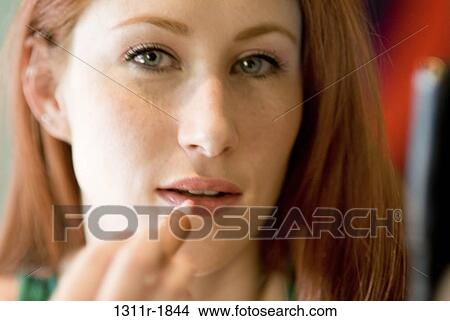 Portrait of a young woman applying lipstick View Large Photo Image Picture - Portrait of a young woman applying lipstick. Fotosearch