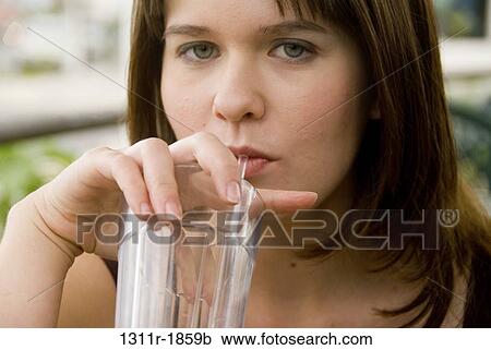Stock Image - Portrait of a young woman sipping cold drink with a drinking straw. Fotosearch