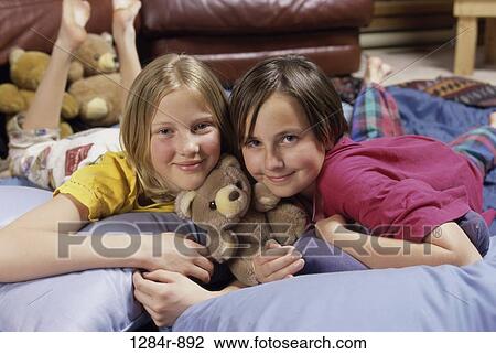 Portrait of two girls lying on a bed View Large Photo Image Stock Image - Portrait of two girls lying on a bed. Fotosearch