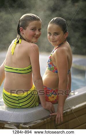 Picture - Rear view of two girls sitting at the edge of a swimming pool. Fotosearch