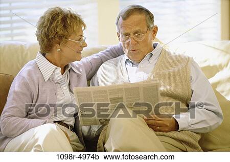 Senior couple sitting on a couch reading a newspaper View Large Photo Image Stock Image - Senior couple sitting on a couch reading a newspaper. Fotosearch