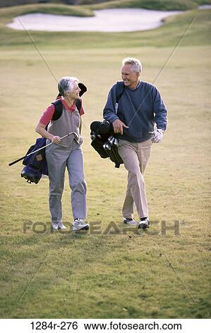 Stock Photograph - Senior couple walking on a golf course holding golf bags. Fotosearch