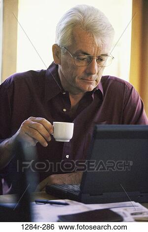 Senior man sitting in front of a laptop computer View Large Photo Image Stock Photograph - Senior man sitting in front of a laptop computer. Fotosearch
