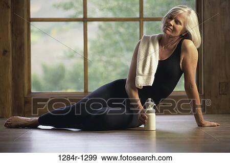 Senior woman sitting on the floor holding a bottle View Large Photo Image Stock Photo - Senior woman sitting on the floor holding a bottle. Fotosearch