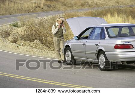 Stock Photo - Senior woman standing in front of a broken down car talking on a mobile phone. Fotosearch