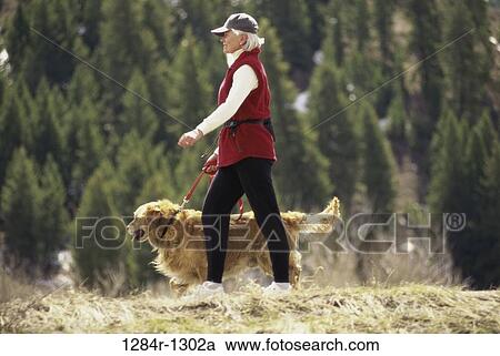 Stock Image - Senior woman walking with her dog in the woods. Fotosearch