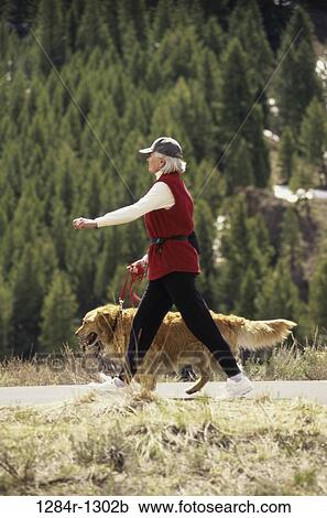 Stock Image - Senior woman walking with her dog in the woods. Fotosearch