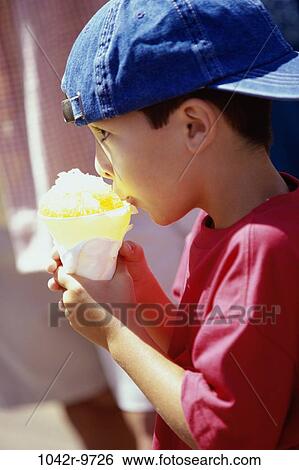Stock Photograph - Side profile of a boy eating a snow cone. Fotosearch
