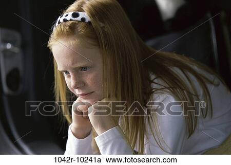 Stock Image - Side profile of a girl sitting with her hands on her chin. Fotosearch