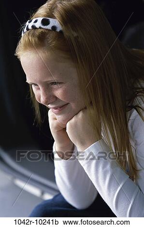 Stock Image - Side profile of a girl sitting with her hands on her chin. Fotosearch