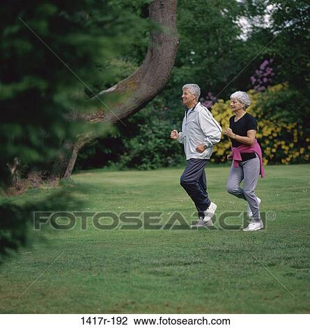 Stock Image - Side profile of a senior couple jogging in a park, Loch Lomond, Scotland. Fotosearch