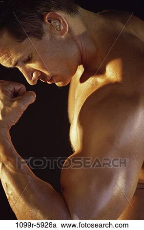 Stock Image - Side profile of a young man flexing his biceps. Fotosearch