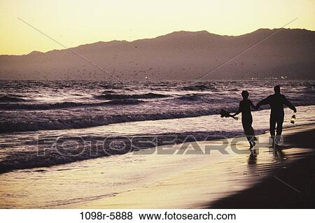 Stock Photo - Silhouette of a young couple running on the beach. Fotosearch
