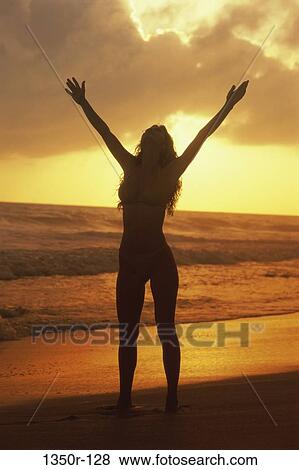 Stock Photo - Silhouette of a young woman standing on the beach during sunset. Fotosearch