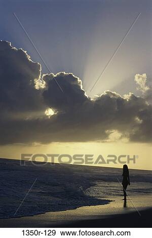 Stock Photo - Silhouette of a young woman standing on the beach. Fotosearch