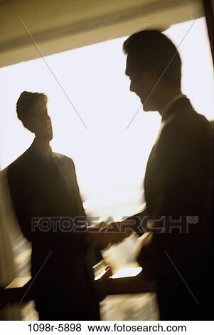Stock Photo - Silhouette of two businessmen shaking hands. Fotosearch