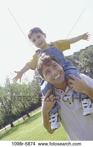 Son sitting on his father's shoulders View Large Photo Image Picture - Son sitting on his father's shoulders. Fotosearch