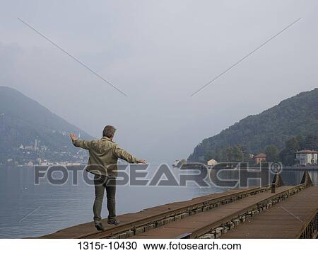 Switzerland, Ticino, Lake Lugano, Man balancing along rail near lake edge View Large Photo Image Stock Image - Switzerland, Ticino, Lake Lugano, Man balancing along rail near lake edge. Fotosearch