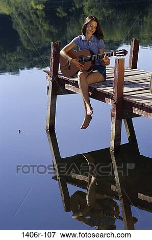 Teenage girl sitting on a dock playing the guitar View Large Photo Image Stock Photo - Teenage girl sitting on a dock playing the guitar. Fotosearch