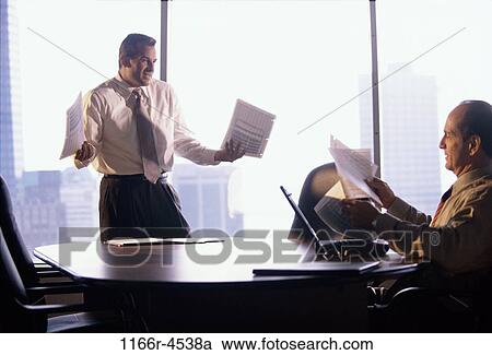 Two businessmen holding documents in an office View Large Photo Image Stock Image - Two businessmen holding documents in an office. Fotosearch