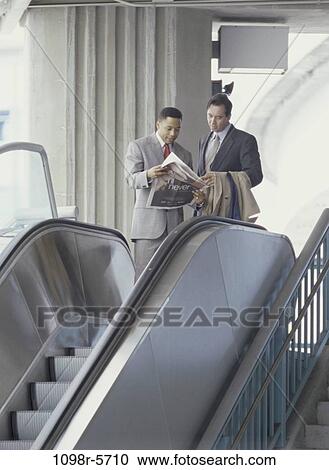 Two businessmen reading a newspaper on an escalator View Large Photo Image Stock Image - Two businessmen reading a newspaper on an escalator. Fotosearch