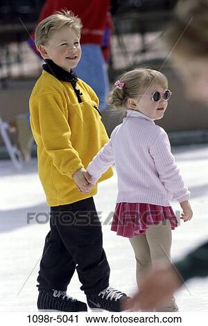 Stock Image - Two children holding hands ice skating. Fotosearch