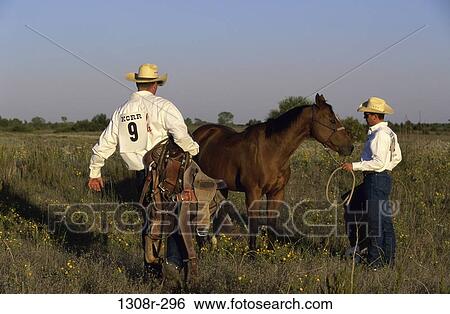Two cowboys standing beside a horse holding a lasso and a saddle View Large Photo Image Stock Photograph - Two cowboys standing beside a horse holding a lasso and a saddle. Fotosearch