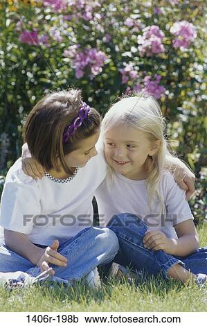 Two girls sitting on a lawn holding each other View Large Photo Image Stock Image - Two girls sitting on a lawn holding each other. Fotosearch