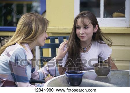 Two teenage girls sitting at a table outdoors View Large Photo Image Stock Image - Two teenage girls sitting at a table outdoors. Fotosearch
