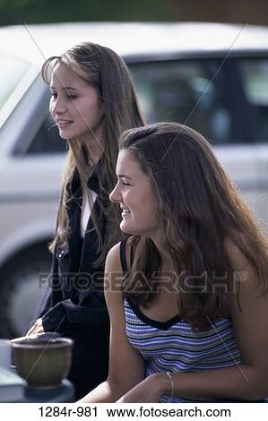 Stock Image - Two teenage girls sitting at a table outdoors. Fotosearch