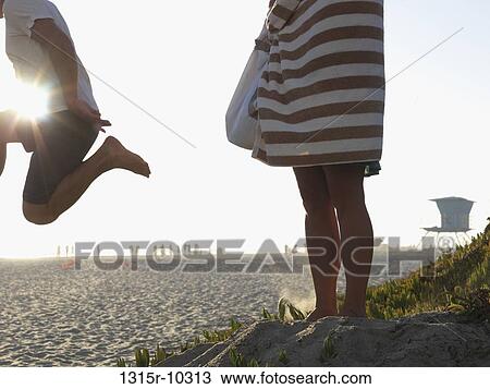 USA, California, San Diego, Man jumping from sand dune while woman watches View Large Photo Image Stock Image - USA, California, San Diego, Man jumping from sand dune while woman watches. Fotosearch