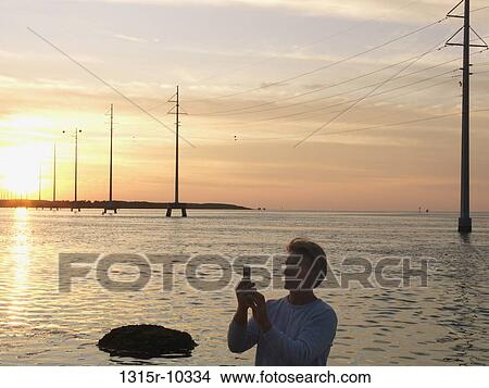 USA, Florida, Keys, Man sending text message below power pylons above sea View Large Photo Image Picture - USA, Florida, Keys, Man sending text message below power pylons above sea. Fotosearch