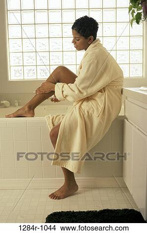 Picture - Woman sitting at the edge of a bathtub wearing a bathrobe. Fotosearch