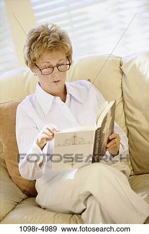 Woman sitting on a couch reading a book View Large Photo Image Stock Photo - Woman sitting on a couch reading a book. Fotosearch