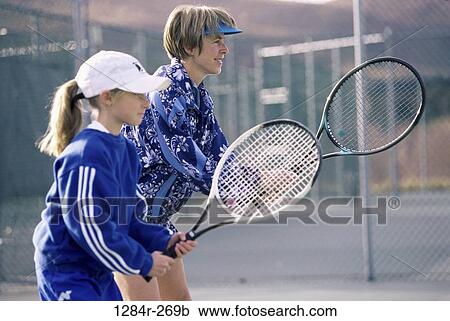 Stock Image - Woman teaching a girl how to play tennis. Fotosearch