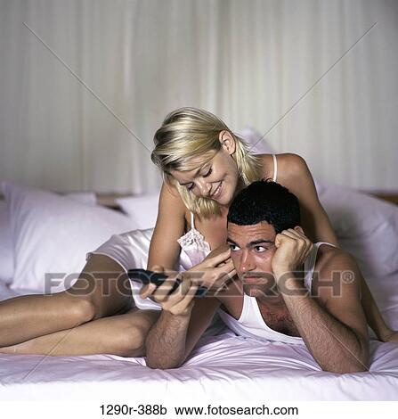 Young couple lying on a bed watching television View Large Photo Image Stock Image - Young couple lying on a bed watching television. Fotosearch