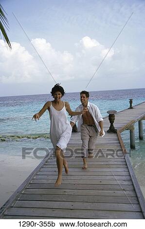 Stock Image - Young couple running on a pier, Maldives. Fotosearch