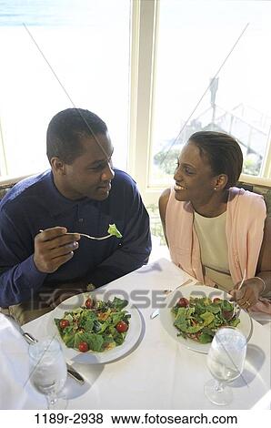 Young couple sitting at a dining table eating salad View Large Photo Image Stock Photo - Young couple sitting at a dining table eating salad. Fotosearch