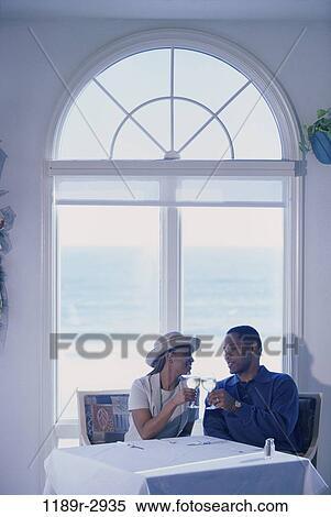 Stock Photography - Young couple sitting at a dining table toasting. Fotosearch