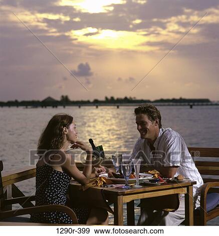 Stock Photo - Young couple sitting together at a dining table, Maldives. Fotosearch