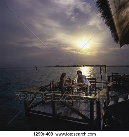 Stock Photo - Young couple sitting together at a dining table, Maldives. Fotosearch