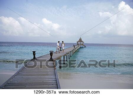 Stock Image - Young couple walking on a pier, Maldives. Fotosearch