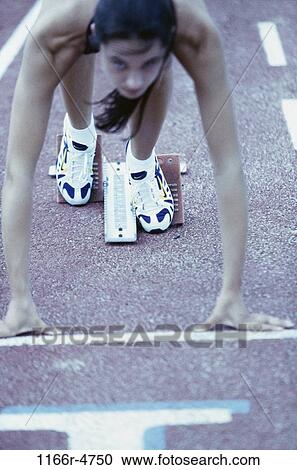 Stock Image - Young female runner at the starting position. Fotosearch