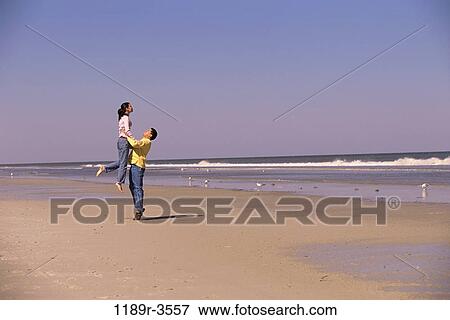 Young man carrying a young woman on the beach View Large Photo Image Stock Photo - Young man carrying a young woman on the beach. Fotosearch