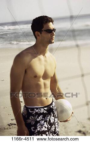 Stock Image - Young man in shorts holding a volleyball. Fotosearch