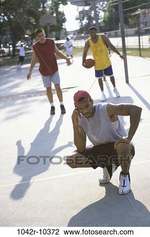 Stock Image - Young man talking on a mobile phone with two young men standing behind him. Fotosearch